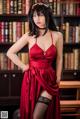 A woman in a red dress posing in front of a bookshelf.