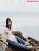 A woman sitting on a rock by the ocean.