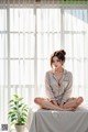 A woman sitting on a bed in front of a window.