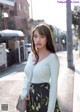 A woman in a blue sweater and floral skirt is walking down the street.