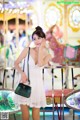 A woman in a white dress standing in front of a carousel.