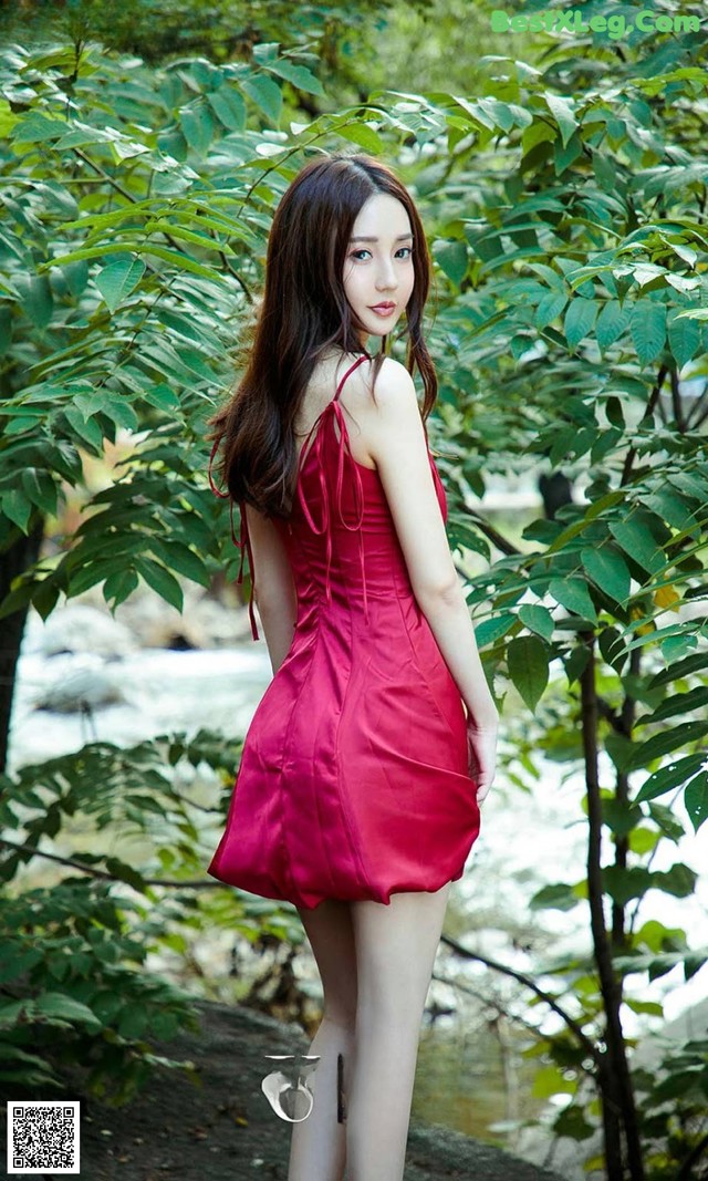 A woman in a red dress standing in the woods.